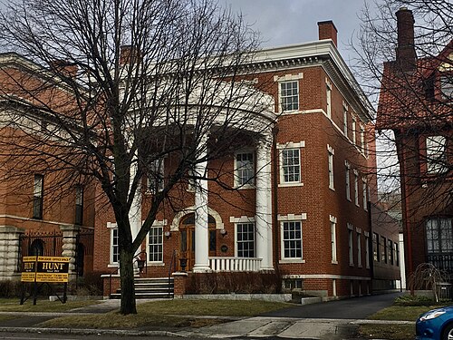 A three storey red brick Colonial Revival house with a bowed two storey Corinthian portico.