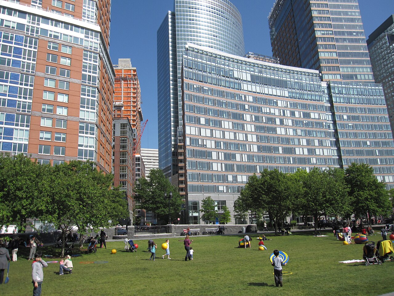 Orange brick and pale stone apartment towers rise over a lawn at the neighborhood's north end, with a construction crane over one building and a curved glass office tower behind.