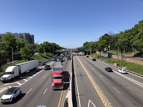 The Gowanus Expressway looking west from the pedestrian overpass at 84th Street, traffic in an open cut with an apartment block on the bank and a bridge tower in the distance.
