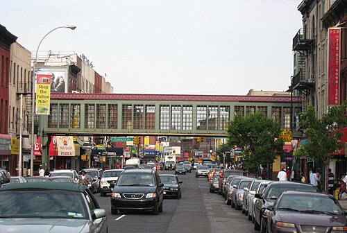 Fulton Street looking east toward Franklin Avenue, storefronts on both sides and the glass walled walkway of the Franklin Avenue station crossing over the street.