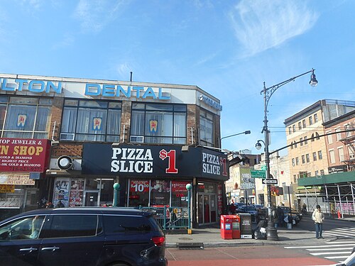 The southwest corner of Nostrand Avenue and Fulton Street, a dollar slice awning under a dental sign, with a pawn shop next door and an old painted record shop sign further along.