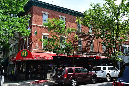 Mezza Luna Pizza at the corner of Arthur Avenue and East 187th Street, red awnings wrapping a three story brick corner building.