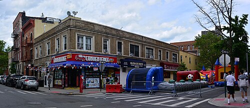 A church street carnival closing East 189th Street at Hughes Avenue, inflatable rides in the roadway and a corner convenience store behind them.