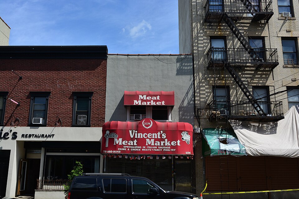 The butcher shop at 2374 Arthur Avenue, trading as Vincent's Meat Market, red awnings over the shopfront and a brick apartment house with fire escapes beside it.