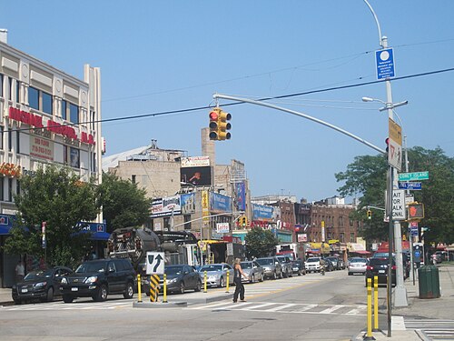 Brighton Beach Avenue looking east from the corner of Coney Island Avenue, two and three storey buildings on both sides with signs and awnings hung out over the sidewalk.