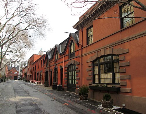 Grace Court Alley on a wet winter day, a one lane mews of orange brick carriage houses with wide arched doorways, dormers in the roofs and no cars on it.