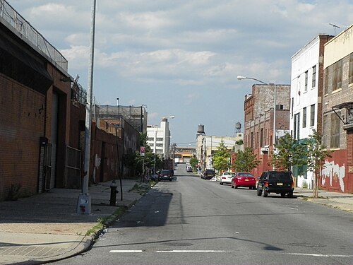 An industrial block with loading bays and roll down shutters, brick warehouses on both sides and water towers on the roofs.