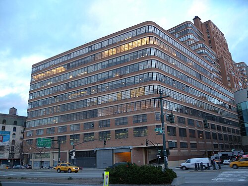 The Starrett-Lehigh Building near sunset, long bands of steel windows and brick curving round the corner, traffic on the highway in front of it.