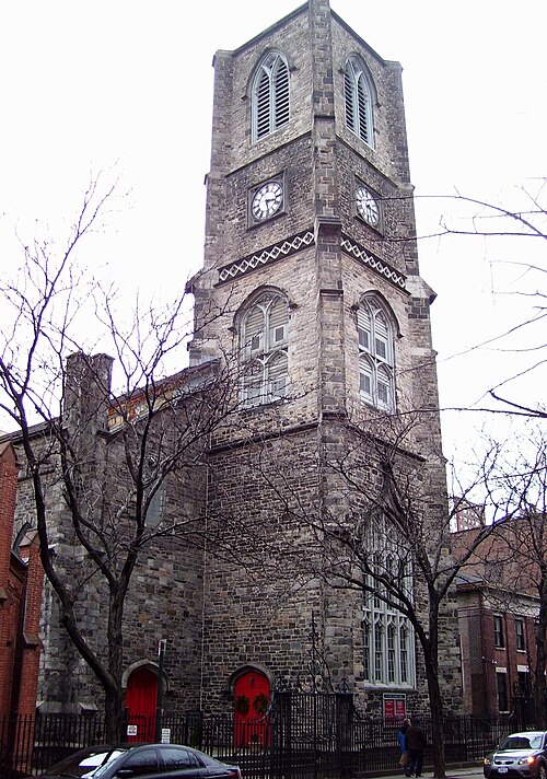 St. Peter's Episcopal Church on West 20th Street, a stone church with a square clock tower and red doors, bare trees in front of it.