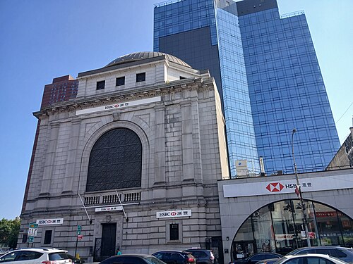 The Citizens Savings Bank building at 58 Bowery, a domed limestone bank with a tall arched window, now carrying HSBC signs, with a blue glass tower behind it.