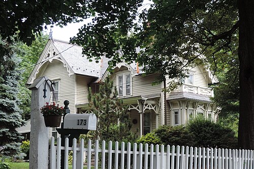 A clapboard Victorian house on Belden Street, scrollwork in the gables and a white picket fence along the sidewalk.