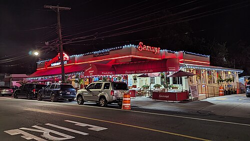 Sammy's Shrimp Box at night, neon signs and strings of lights over the sidewalk tables.