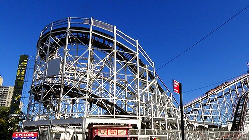 The Cyclone's white wooden lattice and banked first turn against deep blue sky, the vertical CYCLONE sign at left and the red Cyclone Tickets sign at the entrance below.