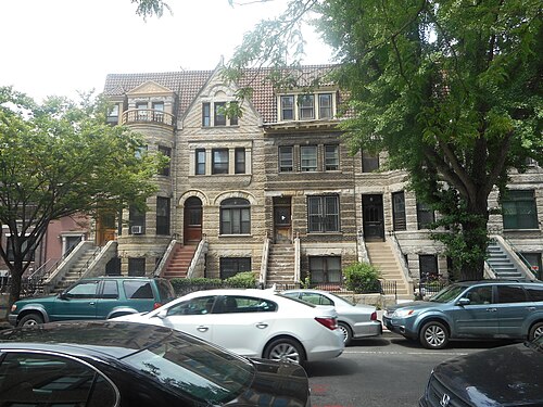 Rowhouses at 1189 to 1195 Bergen Street in rough faced limestone, with tiled roofs, a gable over one house and high stoops down to the sidewalk.