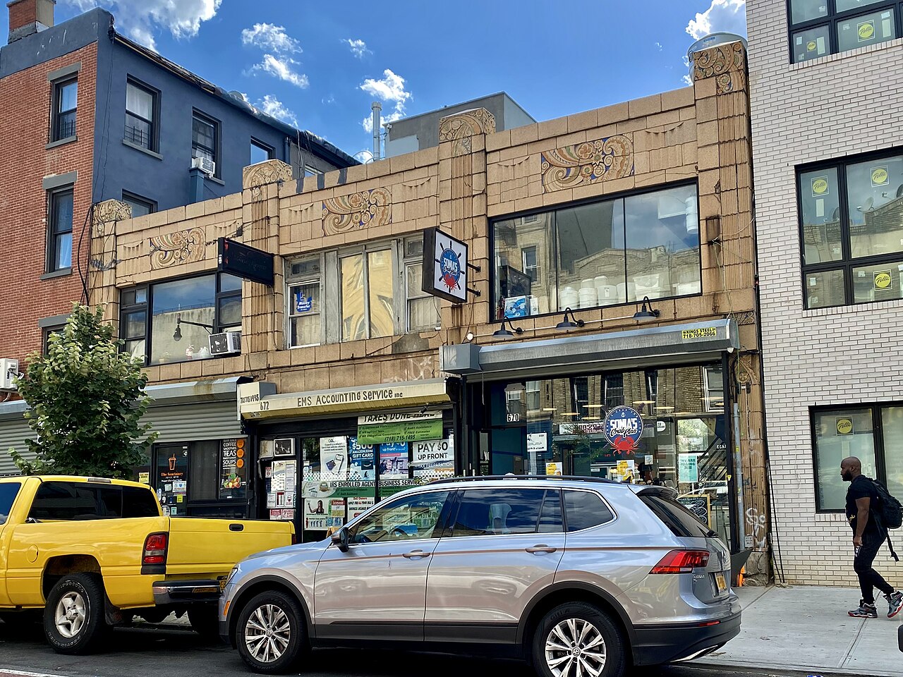 The two floor building at 670 to 674 Nostrand Avenue, its upper front in buff terracotta with painted foliate panels, and an accountant and a seafood counter in the shops below.