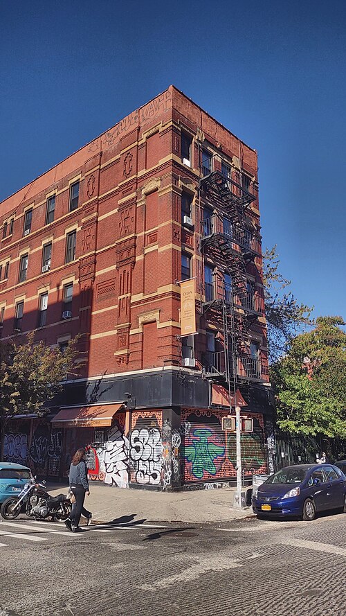 The former Loew's Avenue B Theatre, a brick corner building with terracotta panels and roll down shutters covered in graffiti at street level.