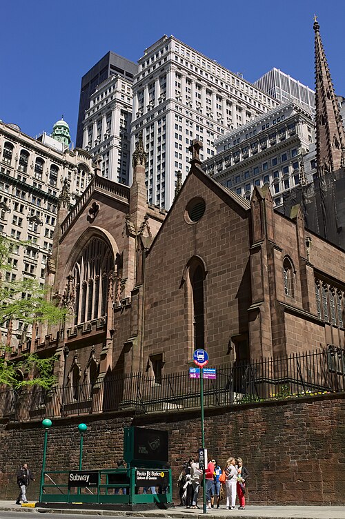 Trinity Church from Trinity Place, the brownstone flank and spire above the churchyard wall, the Rector Street subway entrance at the pavement below.