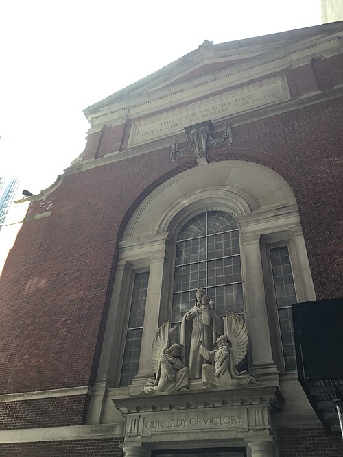 The front of Our Lady of Victory on William Street, red brick with a carved Virgin and two angels over the door.