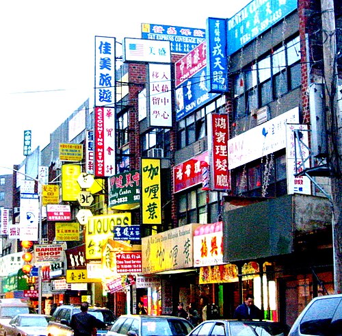 A side street off Main Street a block from the railroad, where the building fronts are covered in projecting and stacked signs for a dental center, a travel service, an accounting office, a barber and a liquor store.