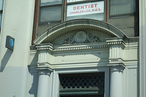 The doorway of 39-15 Main Street at Roosevelt Avenue, an arched stone pediment with a carved tree in the cartouche over paired columns, and a dentist's window sign on the floor above.