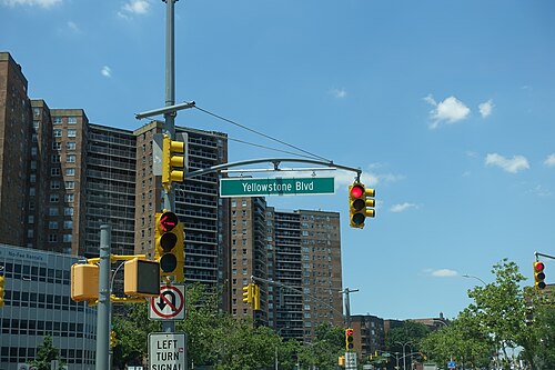 A green street sign for Yellowstone Boulevard hung over the road, brick apartment towers behind it against a clear sky.