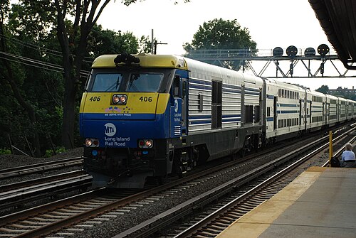 A Long Island Rail Road train arriving at the Forest Hills station, signal lights and trees along the tracks.