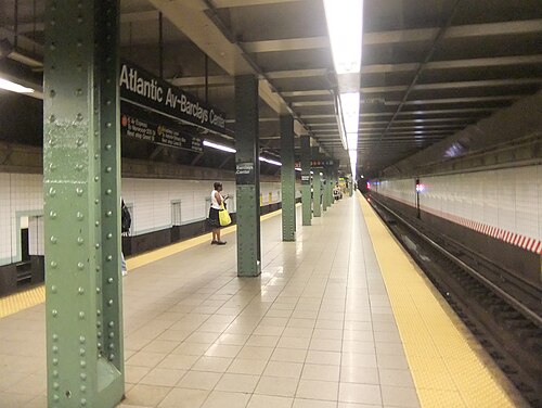 The northbound platform at Atlantic Avenue and Barclays Center, green riveted columns and white tile, with a train's headlights down the tunnel.