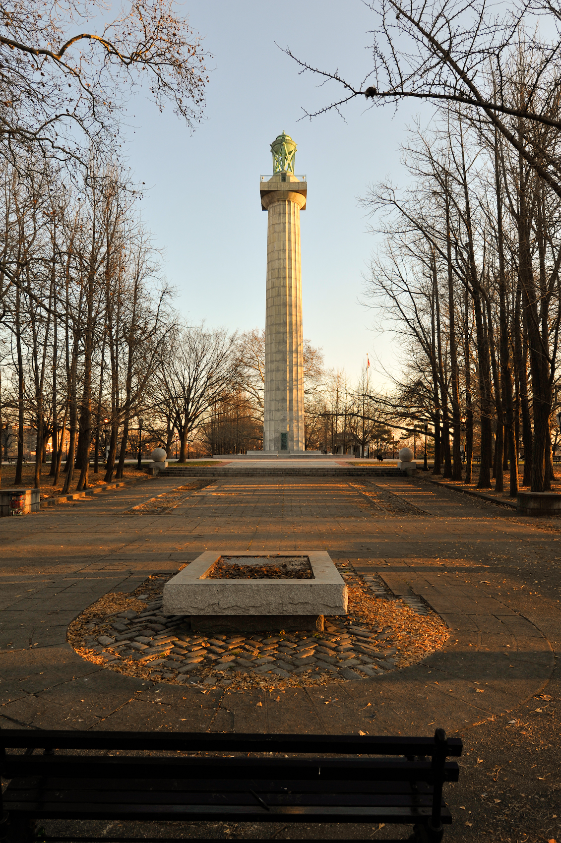 The Prison Ship Martyrs' Monument at the top of Fort Greene Park, a granite column with a bronze lantern on it, seen down the paved plaza in low winter sun.