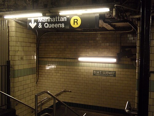 An old B.M.T. Subway sign in tile above a stairway at the Ninth Street transfer, a Manhattan and Queens R sign hung in front of it.
