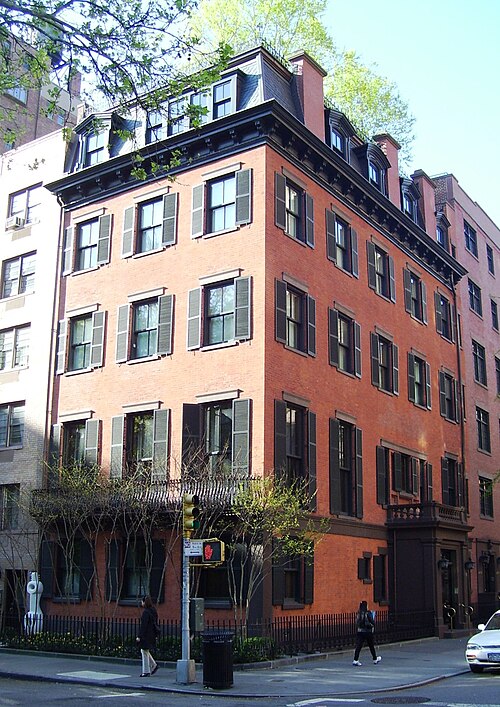 A red brick corner mansion at Irving Place, black shutters on every window, a slate mansard roof and dormers, an iron fence at the sidewalk and a traffic light on the corner.
