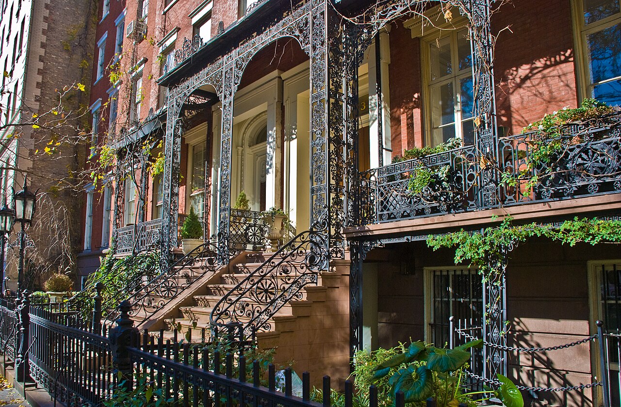 A cast iron portico over a rowhouse stoop, ivy climbing the railings and the scrollwork repeating in the balcony above the door.