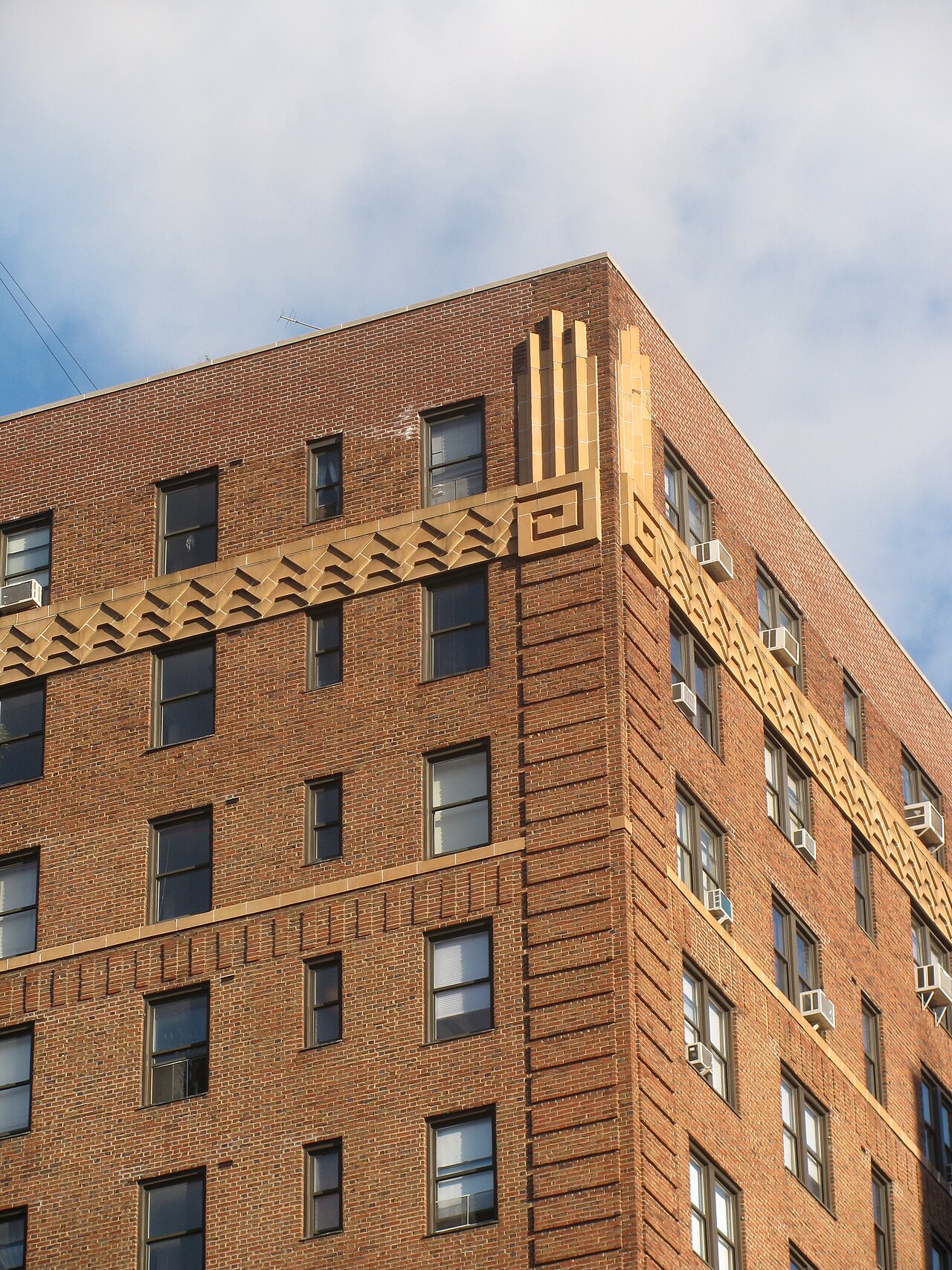 The corner of a brick apartment building with a zigzag terracotta cornice band and pilasters marking the corner edge.