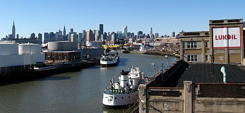 Tug and tankers on Newtown Creek with the skyline behind.