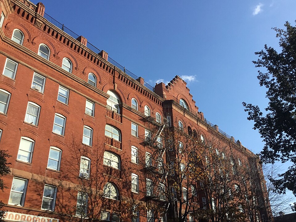 The Astral Apartments on Franklin Street, a long red brick block from the 1880s with iron fire escapes and a laundromat sign at street level.