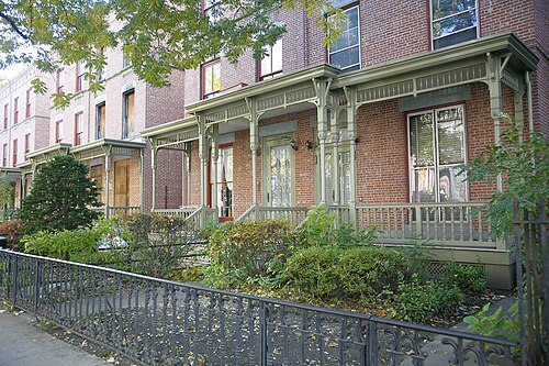 Astor Row wooden porches up close, green columns and front gardens.