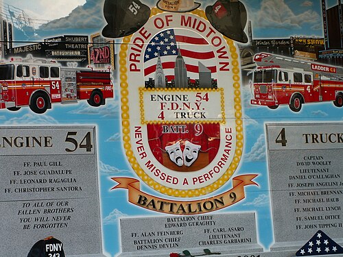 The memorial wall at Engine 54 on Eighth Avenue, painted with theatre marquees and fire trucks, the names of the fifteen members killed on 11 September 2001 cut into the stone beside it.