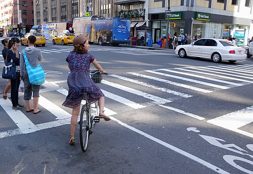 Eighth Avenue at West 50th Street, a cyclist waiting to turn, tour buses on the avenue and a bank on the corner.