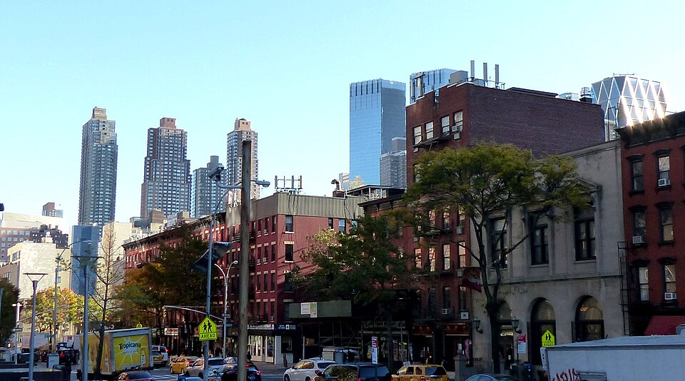 Tenth Avenue between West 50th and West 51st Streets, low brick buildings with storefronts under them and newer West Side towers behind.