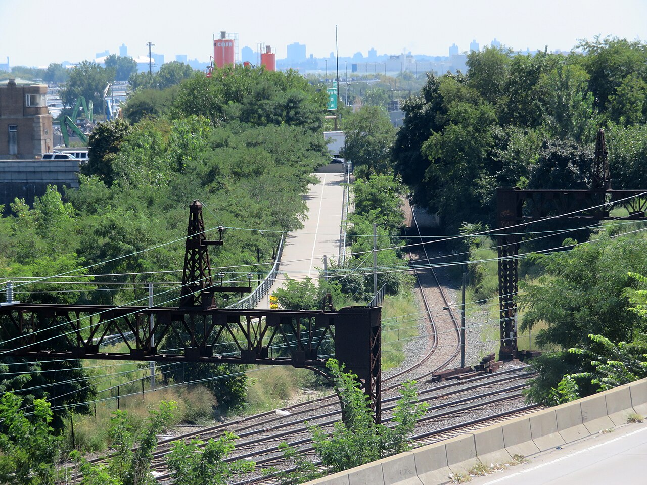 The rail branch into the produce market, tracks curving between trees and steel signal gantries, with red silos and the Manhattan skyline behind.