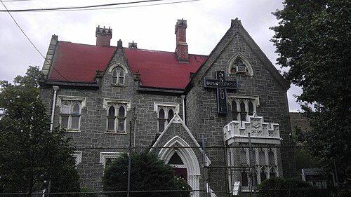Sunnyslope, a gray stone Gothic Revival house with a red roof and two brick chimneys, now Bright Temple A.M.E. Church, behind a chain link fence.