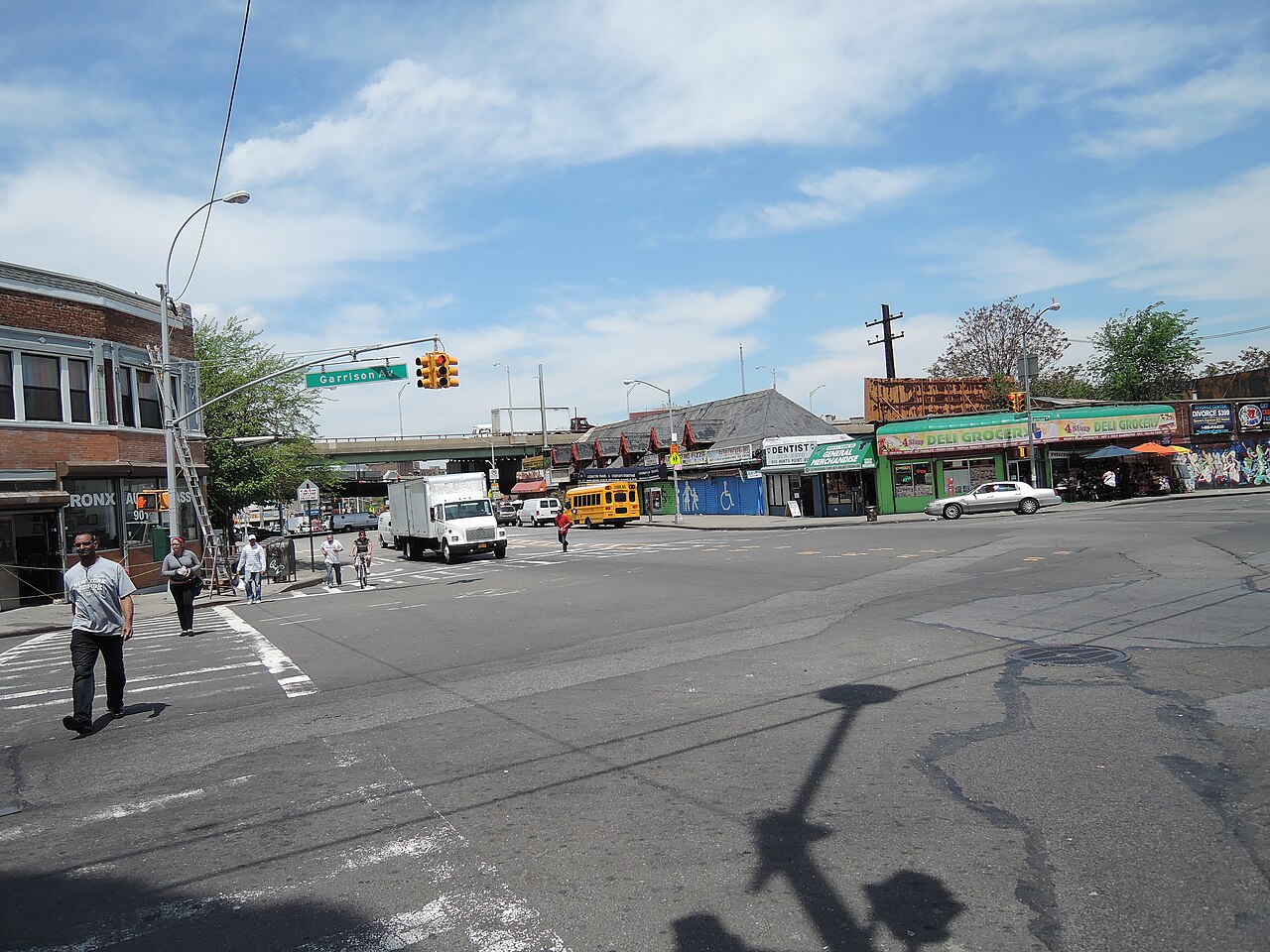 Hunts Point Avenue at Garrison Avenue, storefronts under the old railroad station building, a delivery truck and a school bus stopped at the light.