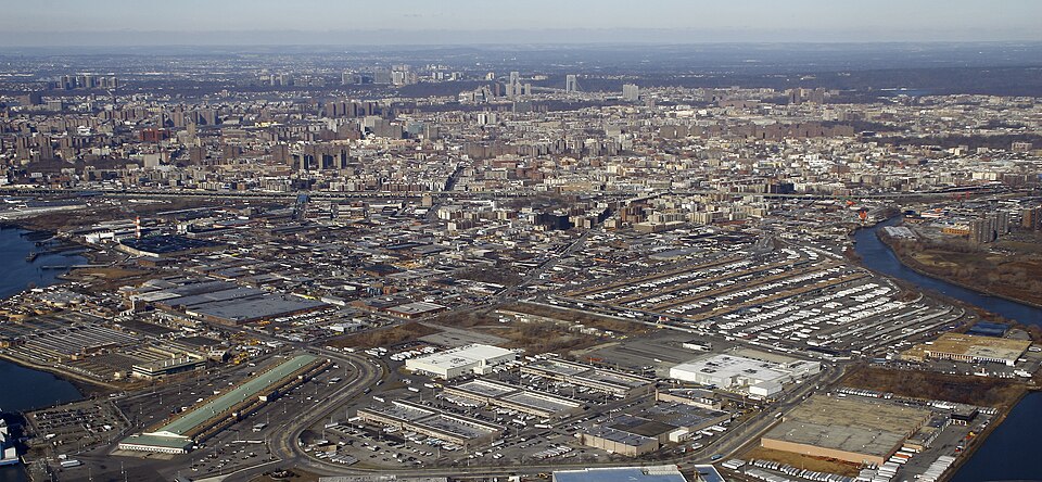 An aerial view over Hunts Point, the fish and produce market's low buildings and parking lots below, the Bronx River at left, upper Manhattan and the George Washington Bridge in the distance.