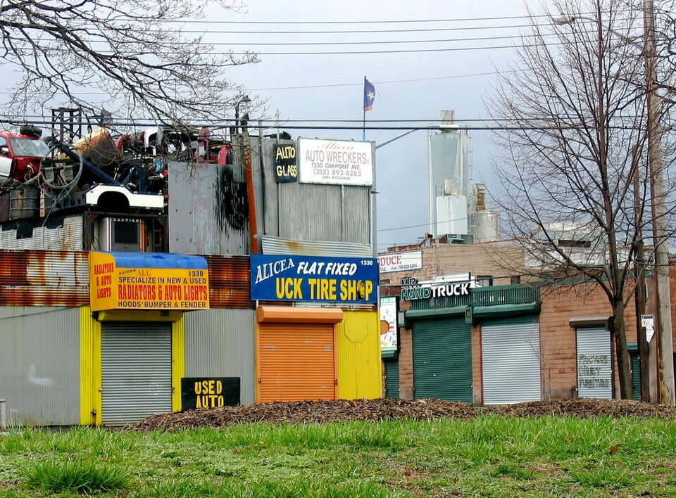 Auto shops on Oak Point Avenue, hand painted signs for auto glass, tire repair and a wrecking yard, junk piled on the roof.
