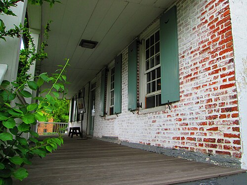 The front porch of the Dyckman House, whitewashed brick with the red showing through, green shutters and a plank floor.