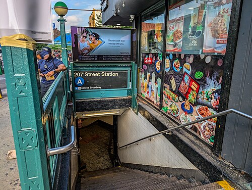 The street stair down to the 207th Street station on the A line, green railings beside a takeout window with photographs of the food on it.
