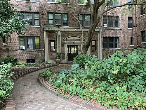The entrance of 78-12 35th Avenue, a brick garden apartment building between 78th and 79th Streets, with a curved brick path and planted beds in front.