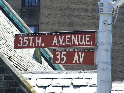 The street sign at 35th Avenue and 81st Street, the avenue's name in Scrabble letter tiles with the point value under each letter, slate roofs behind.