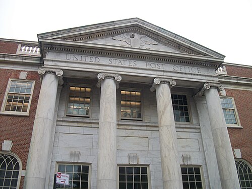 The Jamaica Main post office seen from below, four marble Ionic columns and the words UNITED STATES POST OFFICE carved into the pediment above a stone eagle.