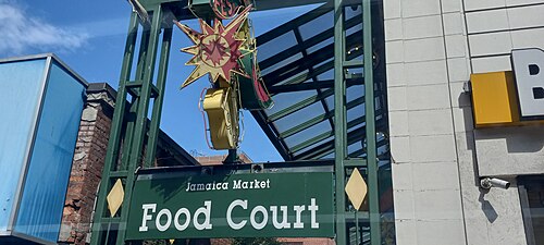 An old marquee sign reading Jamaica Market Food Court, a green steel frame with a starburst light fixture over the entrance.