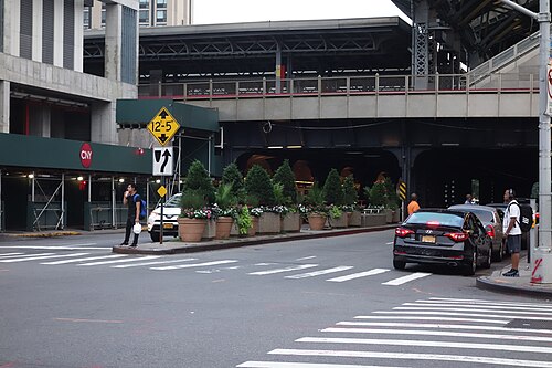 Potted plants in the median of Sutphin Boulevard at Archer Avenue, the concrete underside of the Long Island Rail Road viaduct overhead.